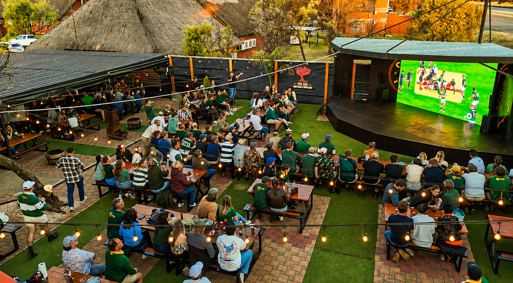A full outdoor crowd watching rugby on Red Oak's big screen.
