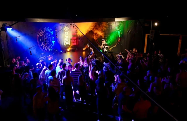 A packed crowd on the Red Oak floor lit by blue and green stage light.