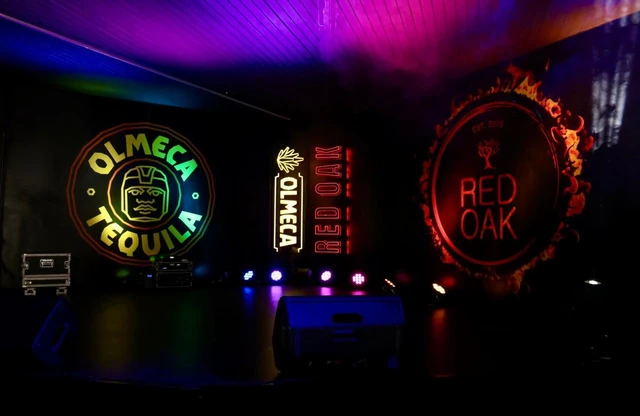 Illuminated Olmeca Tequila and Red Oak signs above the bar at night.