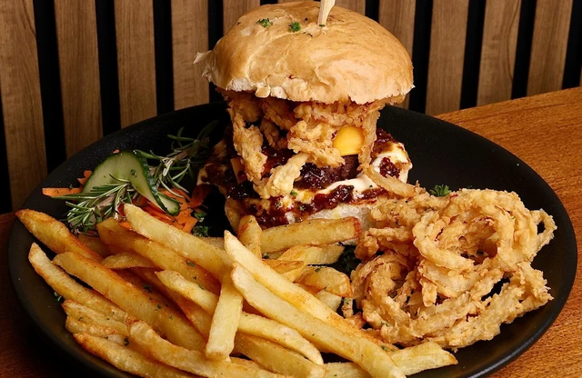 A stacked Red Oak burger with crispy onion rings and chips on a black plate.
