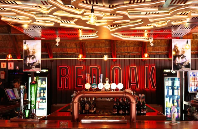 The Red Oak bar counter lit red beneath the sculpted light ceiling.