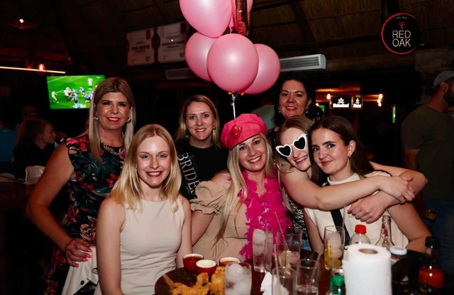A group celebrating at a table decorated with pink balloons.