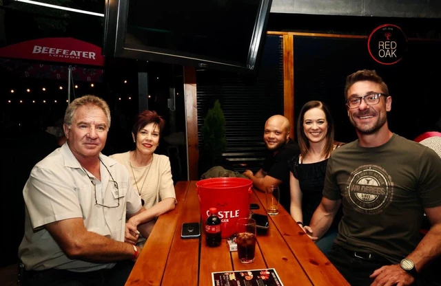 A family group around a timber table with drinks and shot glasses.