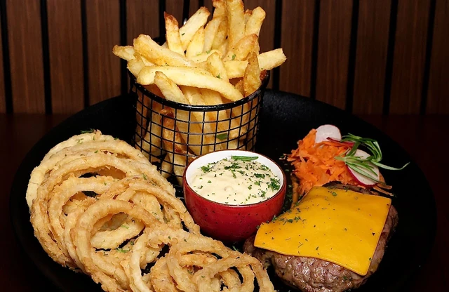 A basket of chips with crispy onion rings, dips and a burger.