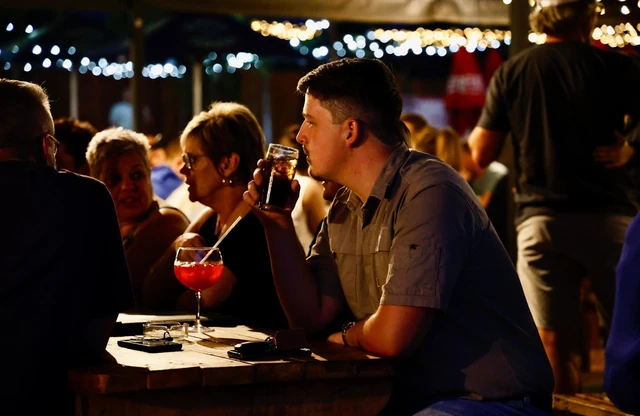 Guests with cocktails at a table under the outdoor lights.