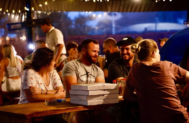A long table of guests sharing pizzas outside.