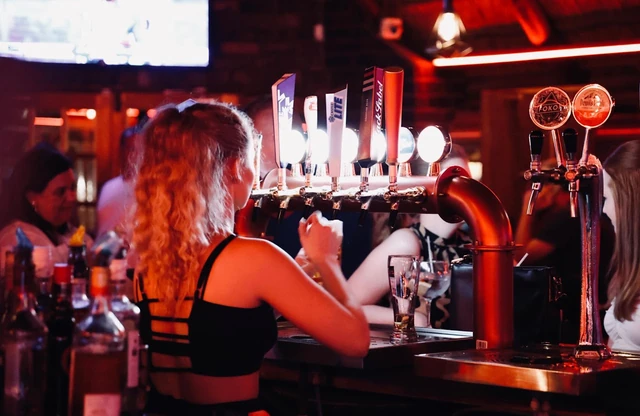 A guest at the bar taps under deep red light.
