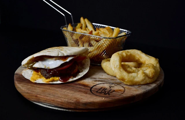 A burger with a basket of fries and onion rings on a Red Oak board.