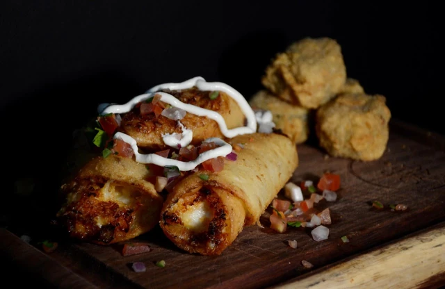 Chicken flautas with dips served on a wooden board.