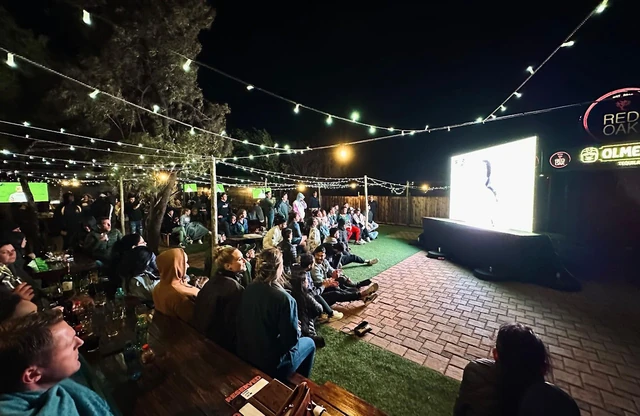 An outdoor screening night with guests seated on the grass and benches.