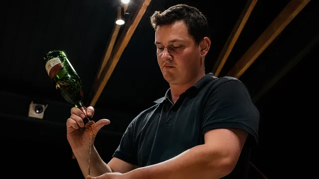 A bartender pouring a drink from a bottle into a metal jigger.