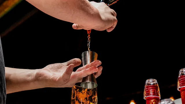 Close-up of spirits being poured into a jigger with a Red Oak glass below.