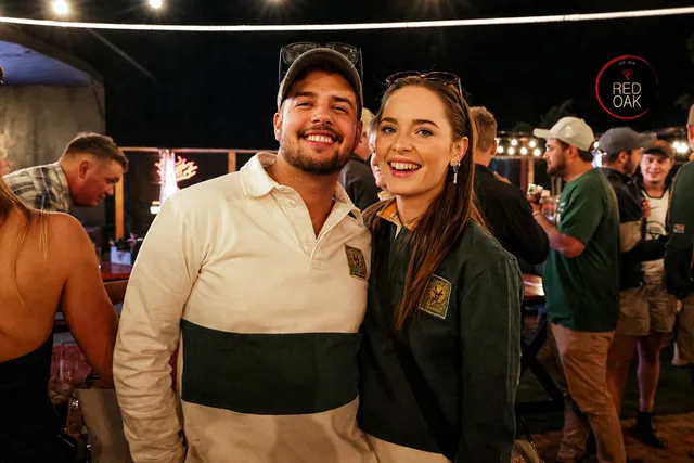 A couple in Springbok rugby jerseys smiling together at Red Oak at night.