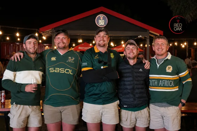 Four friends in Springbok and South Africa rugby jerseys posing together under the lights.