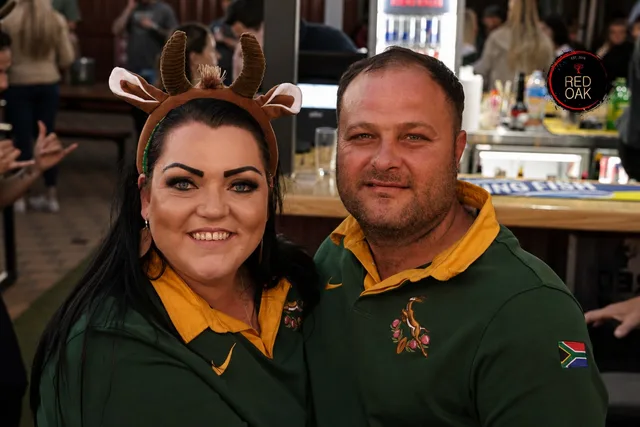 A woman wearing reindeer antlers and a man in a Springbok jersey at the bar.