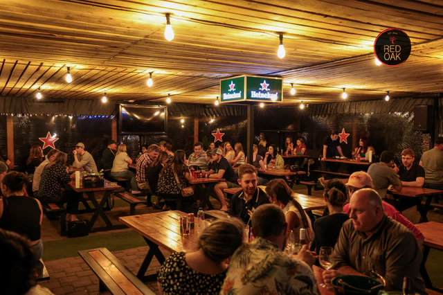A full crowd seated at picnic tables under warm lights in Red Oak's covered outdoor area.