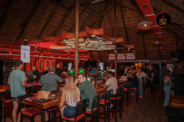 Guests gathered around the Red Oak bar beneath the thatched roof and red neon lighting.